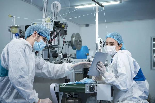 Staff and workers at the mask factory are monitoring the operation of the machines. A mask is being produced on the road. Factory workers are discussing.