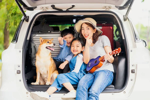Happy family with Shiba inu dog near car outdoors. A family with a mother, daughter and son playing music in the back of the car with Shiba Inu.