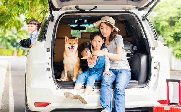 Happy family with Shiba inu dog near car outdoors. A family with a mother, daughter and son playing Paper plane in the back of the car with Shiba Inu.