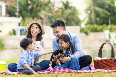 An Asian family plays with a Shiba Inu dog. Happy family with pet dog at picnic in a sunny day. clipart