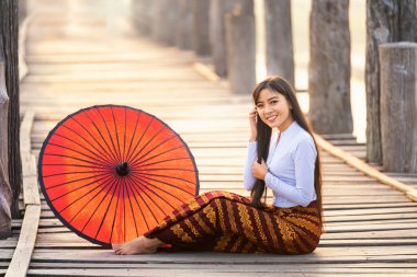 Mandalay Bölgesi 'ndeki Taungthaman Gölü' ndeki U Bein meşe köprüsünde geleneksel kırmızı şemsiyeli genç bir Burmalı kadın. Myanmar..