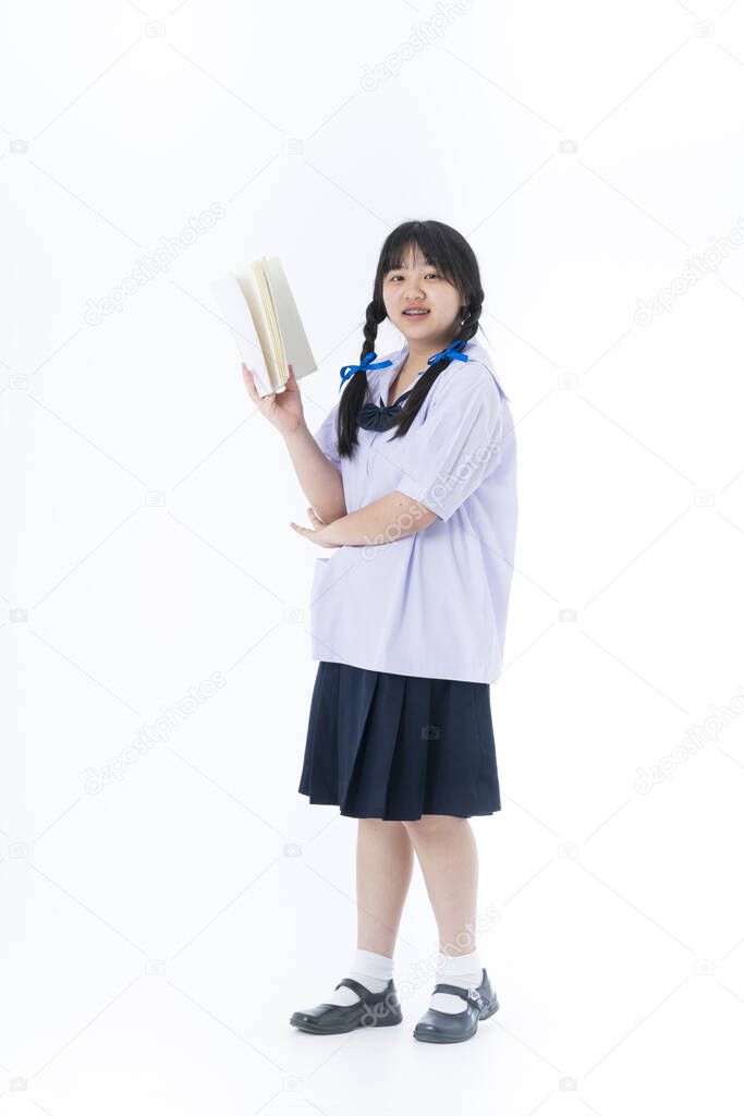 A girl in a school uniform is reading a book on the white background. 