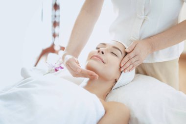 Kadın masaj terapisti kaplıcada masaj yapıyor. Genç bir kadın spa salonunda kafa ve yüz masajı yaptırıyor..