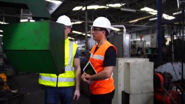 Fabrika atölyesinde otomatik robot makinelerinin ürünlerini üretmek için güvenlik şapkası komutu bilgisayarı takan işçiler.