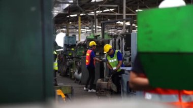 Fabrika atölyesinde güvenlik şapkası takan işçiler. Asya makine mühendisi endüstriyel torna makinesini çalıştırıyor.