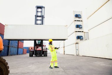 İthalat ve İhracat konsepti. Foreman, malları yükleme limanında dizüstü bilgisayar kullanıyor. Depoda güvenlik ekipmanlarıyla çalışan bir işadamı..