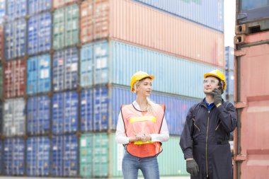 Güvenlik kıyafeti giyen ustabaşı telsiz iletişimi kullanarak konteynırdaki malların hareketini kontrol ediyor. Mühendisler mal yükleme limanında cep telefonu kullanıyorlar.