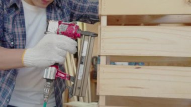 Marangoz elinde matkap makinesiyle tezgahta duruyor. Marangoz çivi tabancası kullanıyor.