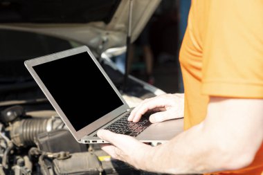 Bir araba tamircisi motor çalışmasını kontrol etmek için dizüstü bilgisayar kullanıyor.. 