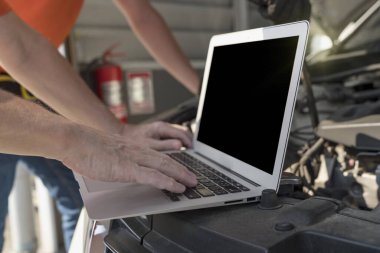 Araba tamiri. Bir araba tamircisi motor çalışmasını kontrol etmek için dizüstü bilgisayar kullanıyor.. 