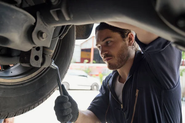 A car mechanic repairing the brakes and shock absorber. Car brake repairing in garage. Auto mechanic hands using wrench to repair a car engine.