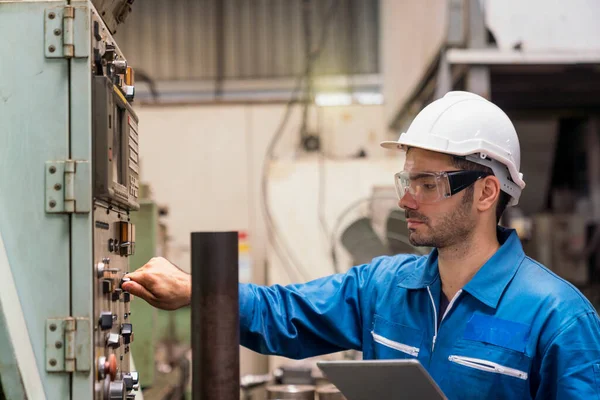 The technician is turning the machine on. Industrial mechanics are working in front of a factory machine.