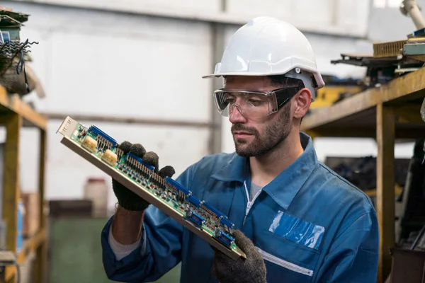 The factory technician is inspecting the electronics in the factory. Industrial mechanics are working in front of a factory machine.