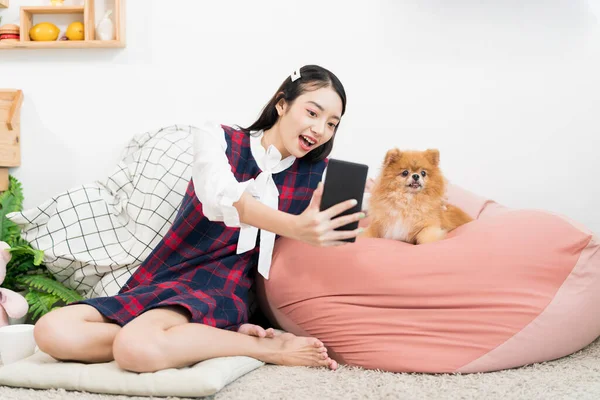 リビングに小さな犬と一緒に携帯電話の自撮りを使用して若い女性 ポメラニア語リビングで女の子と一緒に — ストック写真