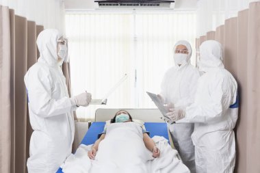 Doktor, hasta yatağında yatarken geçmişini kontrol ediyor. Doktorlar ve çalışanlar COVID 19 'un kontrollü bölge, eyalet karantinasındaki hastaları kontrol edip tedavi etmesini engelleyecek.