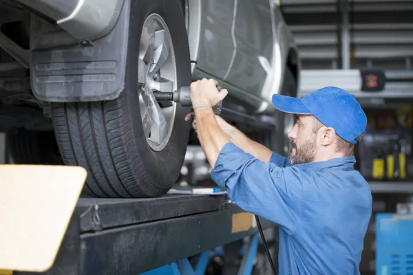 Service repair maintenance concept. Handsome worker in uniform changing car wheel. Male mechanic using rim wrench to fix car tire at auto repair shop.