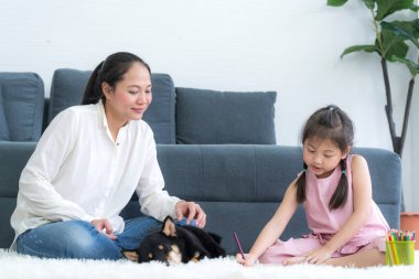 Bir anne kızına oturma odasında Shiba Inu köpeğiyle ödev yapmayı öğretir..