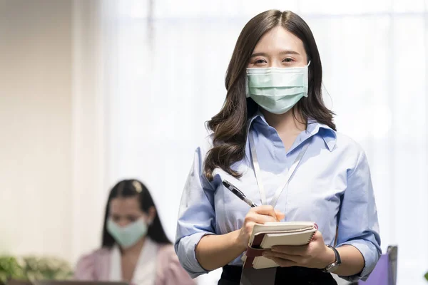 Employees who are recording the meeting. A young worker wearing a mask in the office.