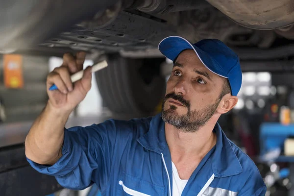 Auto mechanic in work clothes inspects a car in a workshop of a car. A car mechanic holding pen.