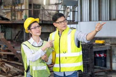 Bir fabrikada iki mühendis. Profesyonel teknisyenler bir tablet bilgisayar tutuyor ve teknisyenler ve mühendisler endüstriyel santrallerde parmaklarını ileri uzatıyorlar..