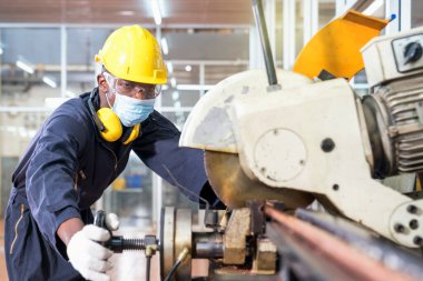 Bir fabrika tamircisi bakır boruları kesmek için elektrikli testere kullanıyor. Uzman bir teknisyen çelik fabrikasındaki endüstriyel makineleri inceliyor..