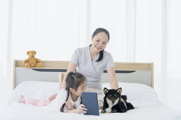黒い芝犬と一緒に寝室のベッドでタブレットを使用して母親と娘を持つ家族 — ストック写真
