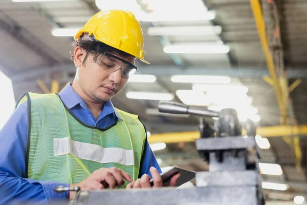 製造業 若い男性労働者は 工場のワークショップで機械を見てタブレットとハード帽子と保護ガラスを身に着けている — ストック写真