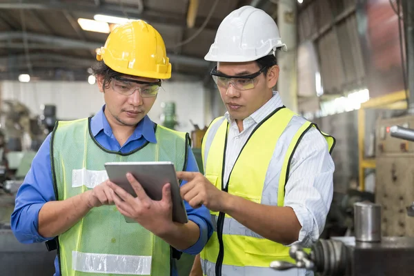 Asian mechanical engineer operating industrial lathe machine. Technicians and engineers are using tablet in industrial.