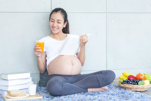 Gravid Kvinna Dricker Apelsinjuice Och Läser Bok Vardagsrummet — Stockfoto