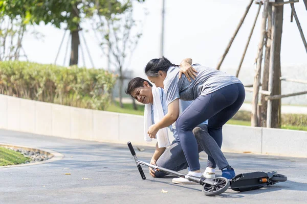 Middle aged woman helping a man who rides a scooter. Old man skating and falling. If you fall, you must use accident insurance.