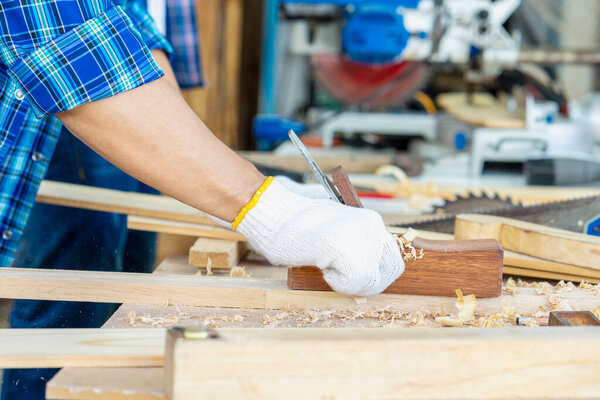 Wood processing at carpentry shop. Carpenter protective glasses treating a wooden bar with a black jack plane.