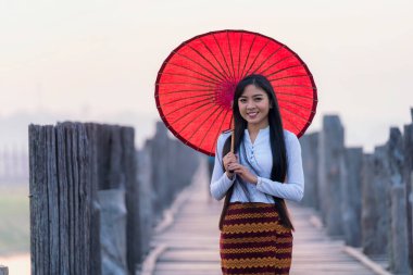 Birmanyalı bir kadın Asya 'nın en uzun meşe köprüsünde kırmızı şemsiyeyle yürüyor. U-bein köprüsü, Mandalay, Myanmar.