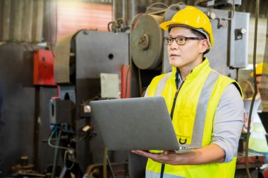 Profesyonel teknisyenler endüstriyel bir fabrikada dizüstü bilgisayarla makineyi kontrol etmeye çalışıyorlar..