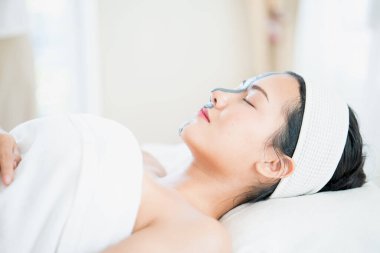 Güzellik merkezinde kilden maske takan genç bir Asyalı kadın. Yüz maskesi yapan bir güzellik uzmanı..