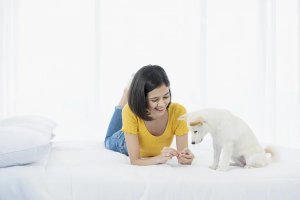白芝犬はベッドで若いアジアの女性の手に食品に興味を持っています — ストック写真