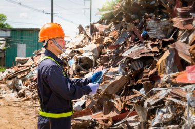 Mühendis ve geri dönüşüm. Geri dönüşüm merkezinde duran mühendisler. Erkek ustabaşı koruyucu ekipman takıyor ve elinde tablet tutuyor..