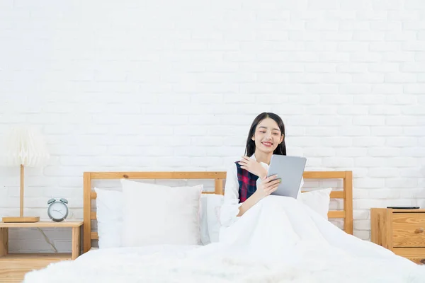 アジアの女性はベッドでタブレットを使っている アジアの女性は朝にベッドの上のタブレットを使用しています — ストック写真