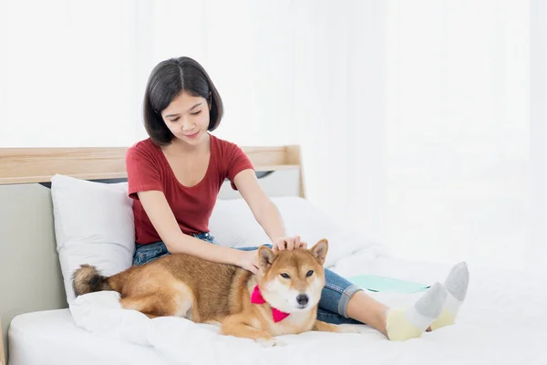 犬と一緒にベッドの上に赤いTシャツを着た若いアジアの女性 女の子とベッドの上で柴犬 — ストック写真