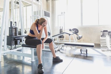 Egzersiz yapmaktan yorgun düşmüş genç bir kadın. Genç kadınlar aşırı egzersizden dolayı kas ağrıları çekiyor..