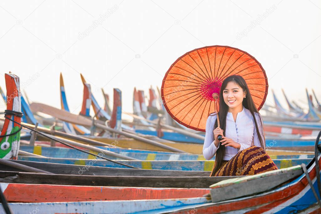 A young Burmese woman holding a red umbrella sitting on a gondola. U-bein bridge, Mandalay, Myanmar.