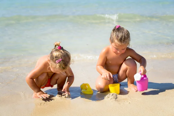 Dos niñas jugando con arena cerca del mar cristalino . — Foto de Stock