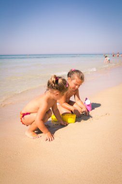 Berrak deniz kenarında kumla oynayan iki küçük kız.