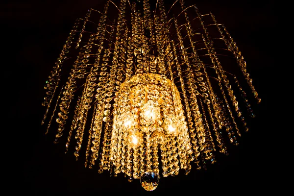 A crystal chandelier glows with golden light — Stock Photo, Image