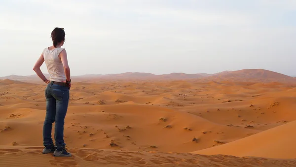 Jovem mulher bonita desfrutando de uma vista incrível sobre o mar dunas vermelhas de Erg Chebbi, com beduínos de camelo no fundo, Marrocos, perto da fronteira com a Argélia — Fotografia de Stock