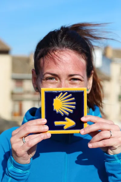 Jeune belle portrait de pèlerine posant avec le carreau bleu typique "Camino de Santiago" peint avec une coquille jaune et une flèche Photo De Stock