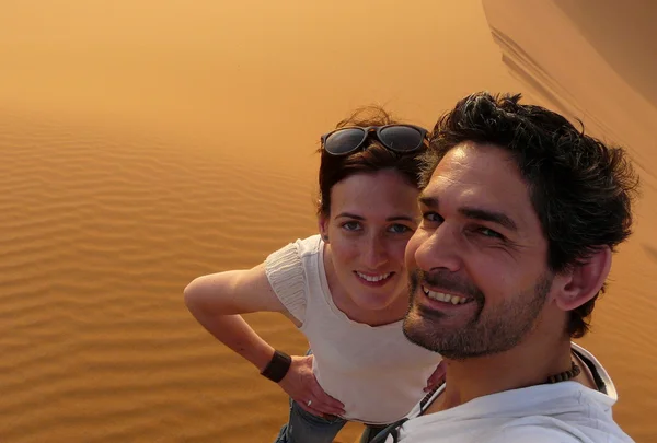 Una joven pareja tomando una foto mientras sube a la cima de la Gran Duna de Arena en el mar de la duna roja de Erg Chebbi, Marruecos . — Foto de Stock