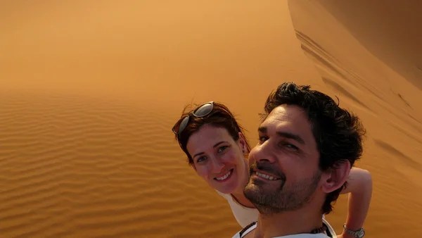 Um jovem casal tirando uma foto de si mesmo enquanto subia ao topo da Grande Duna de Areia no mar de dunas vermelhas de Erg Chebbi, Marrocos . — Fotografia de Stock