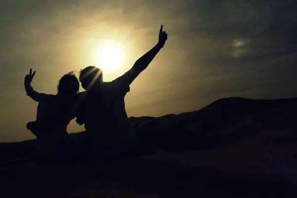 若い冒険家の砂丘の砂の上に座っているとモロッコ シェビ赤い砂丘海を見渡す素晴らしい夕日を楽しむカップル. — ストック写真
