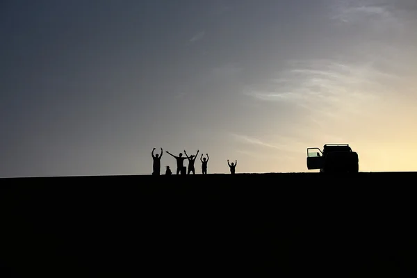 Ένα πακέτο των τυχοδιώκτες χαιρετισμό από την κορυφή του ένα μεγάλο αμμόλοφο απολαμβάνοντας ένα όμορφο καλοκαίρι ηλιοβασίλεμα στη Dakhla όαση, Αίγυπτος. — Φωτογραφία Αρχείου