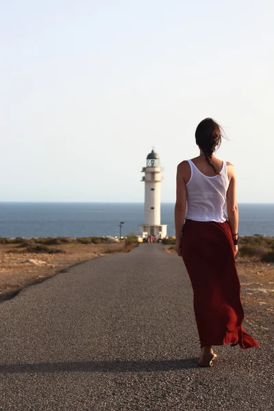 Joven hermosa mujer caminando lentamente hacia el faro del Cap de Barberia durante un increíble atardecer de verano . — Foto de Stock